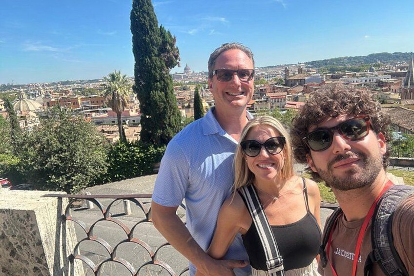 Tres personas de pie en una terraza, con un paisaje urbano al fondo. 3