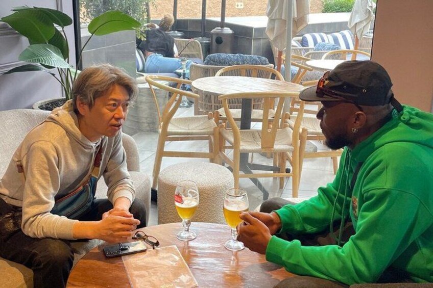 Two people sitting at a table with drinks, in a cafe with outdoor seating. 5