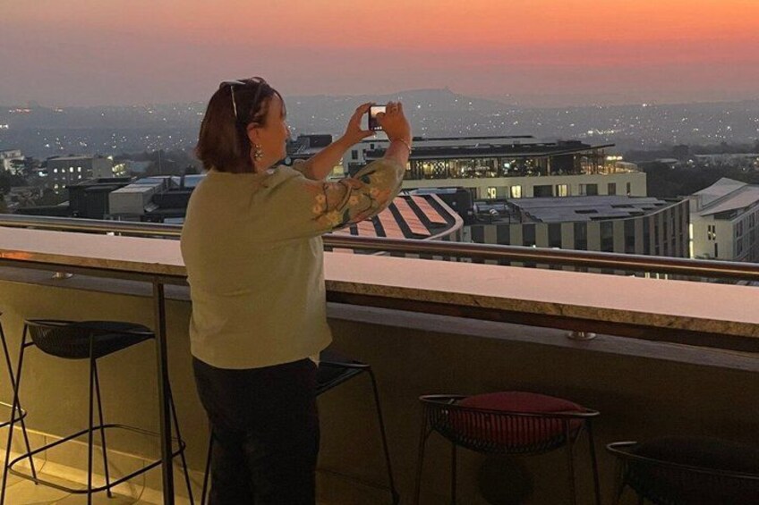 A person taking a photo of a sunset from a balcony with chairs and a railing. 1