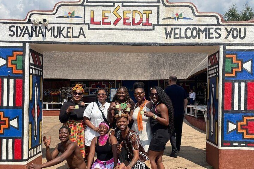 Un grupo de personas posando frente a una entrada colorida con las palabras 'Siyamamukela' y 'Lesedi' escritas en ella. 2