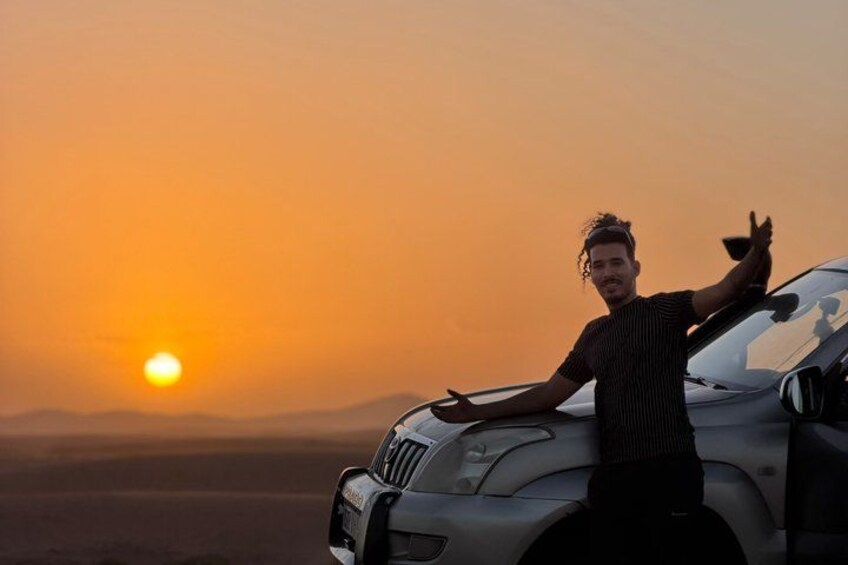 A person standing next to a car with a sunset in the background. 5