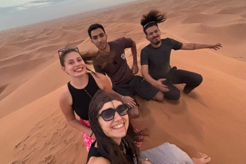 Four people sitting on a sand dune with a desert landscape in the background. 3