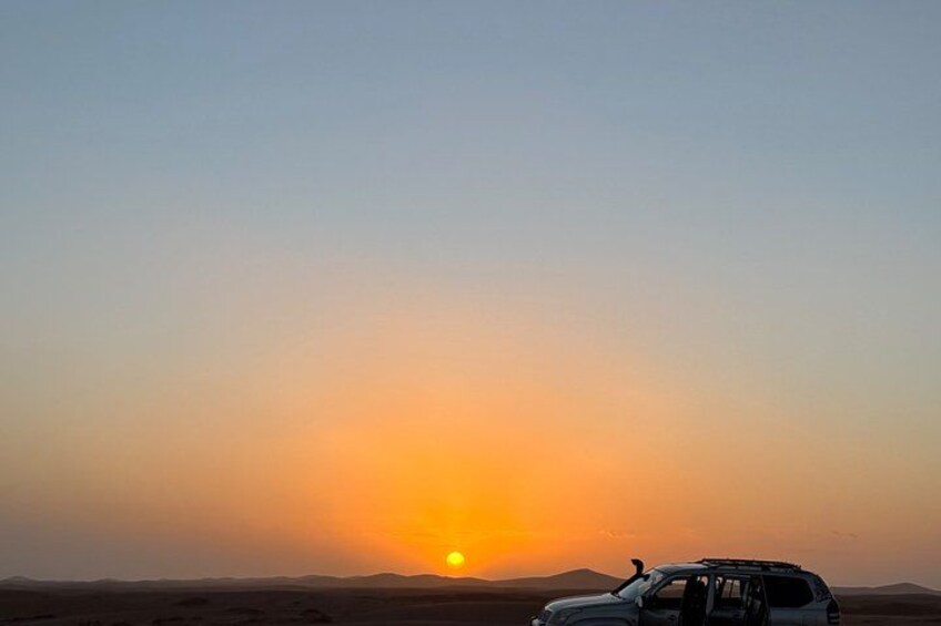 A sunset over a desert landscape with a vehicle in the foreground. 4
