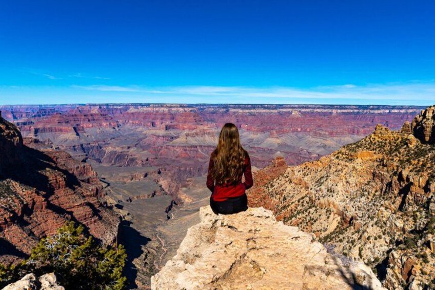 A person sitting on a rocky ledge overlooking a canyon with layered rock formations. 1