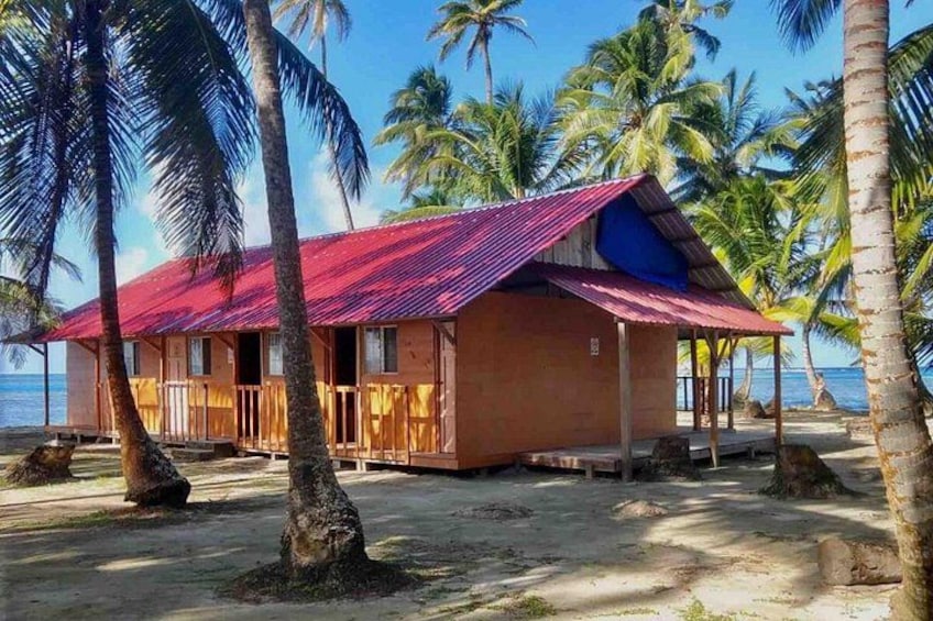 A beach house with a red roof, surrounded by palm trees and the ocean. 5