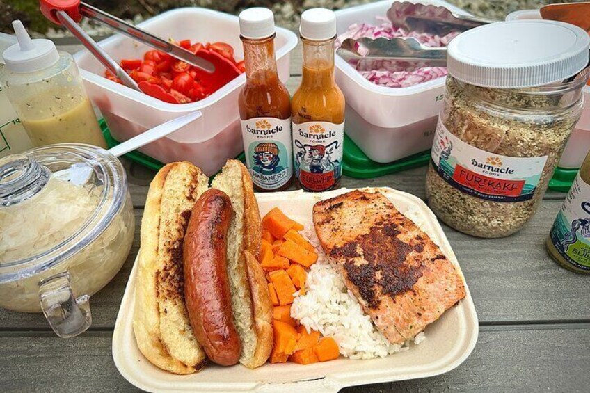 A meal with grilled sausage, salmon, rice, and carrots, along with condiments and sauces. 1