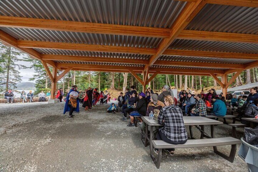 A covered picnic area with people sitting at tables, surrounded by trees. 3