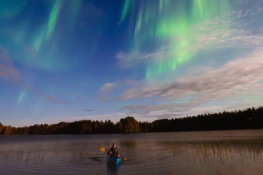 En person som paddlar kajak på en stilla sjö med en skog i bakgrunden och norrsken på himlen. 4