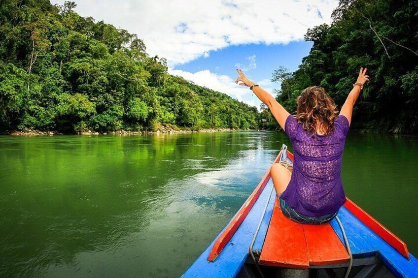 A person on a boat with arms raised, surrounded by a river and dense greenery. 5