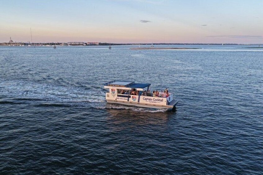 A boat named 'Captain Cocktail' on a body of water with a distant shoreline and a clear sky. 2