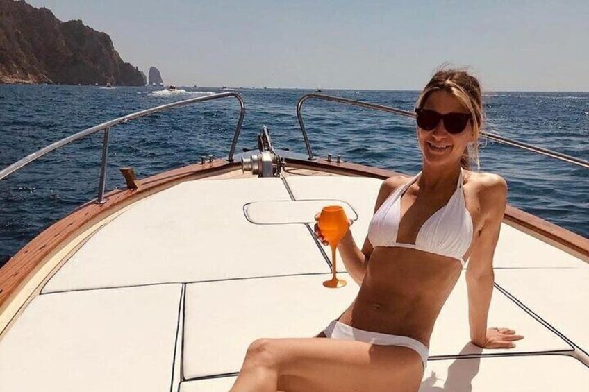 A person on a boat with a drink, rocky coastline, and water. 5