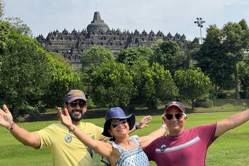 Three people posing with their arms outstretched in front of a large temple complex. 4