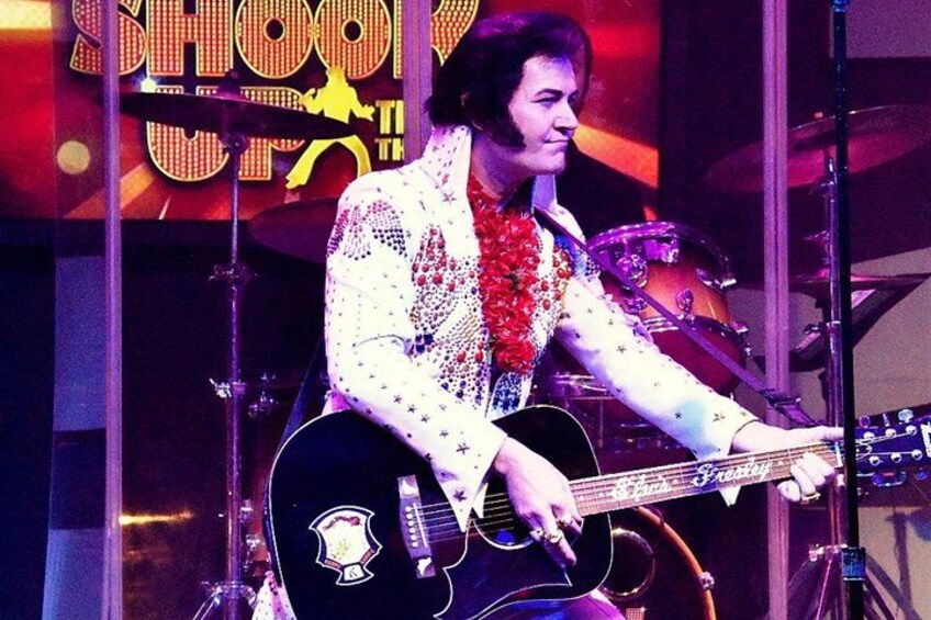 A person playing a guitar on stage with a drum set in the background. 2