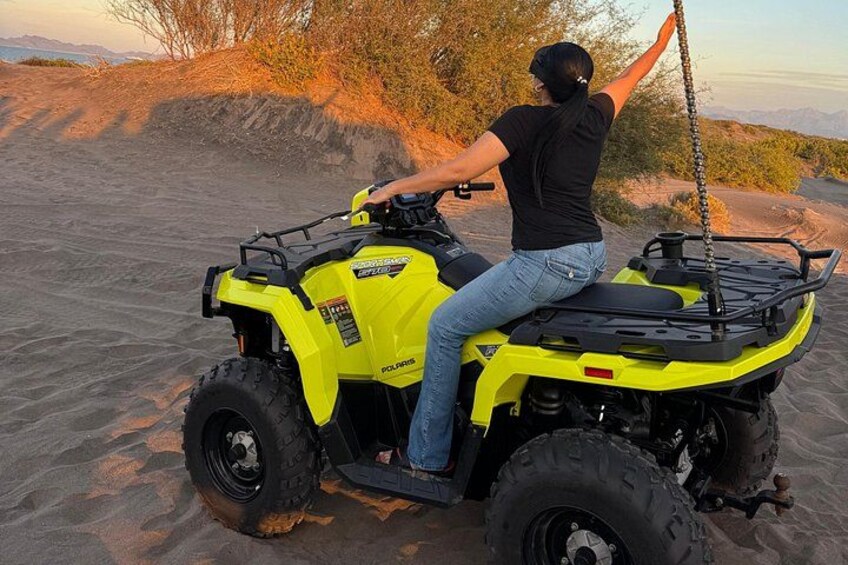 En person kører på en gul Polaris ATV over sandet terræn med sparsom vegetation og fjerne bjerge. 2