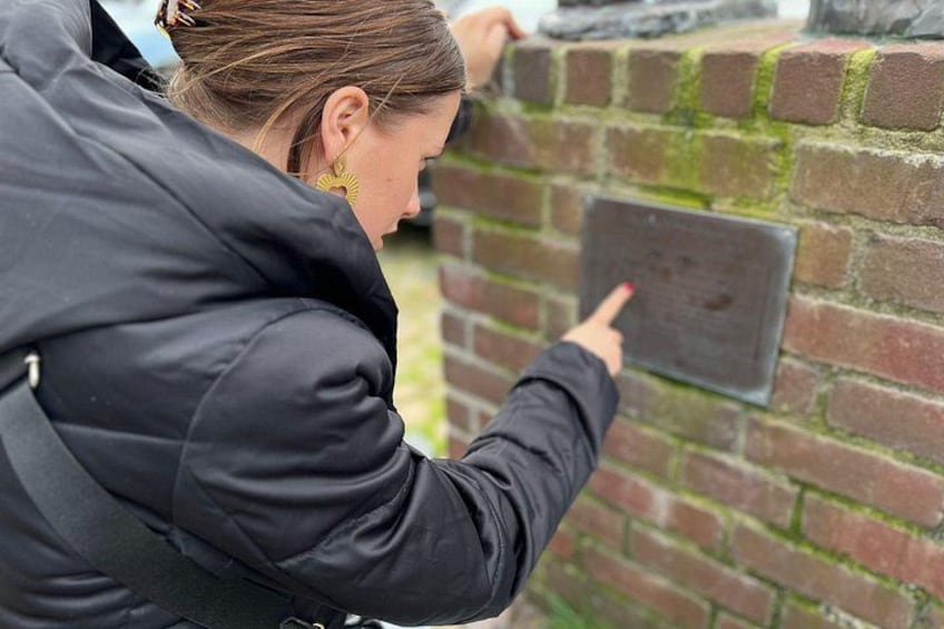 Una persona indica un muro di mattoni con una placca metallica. 1