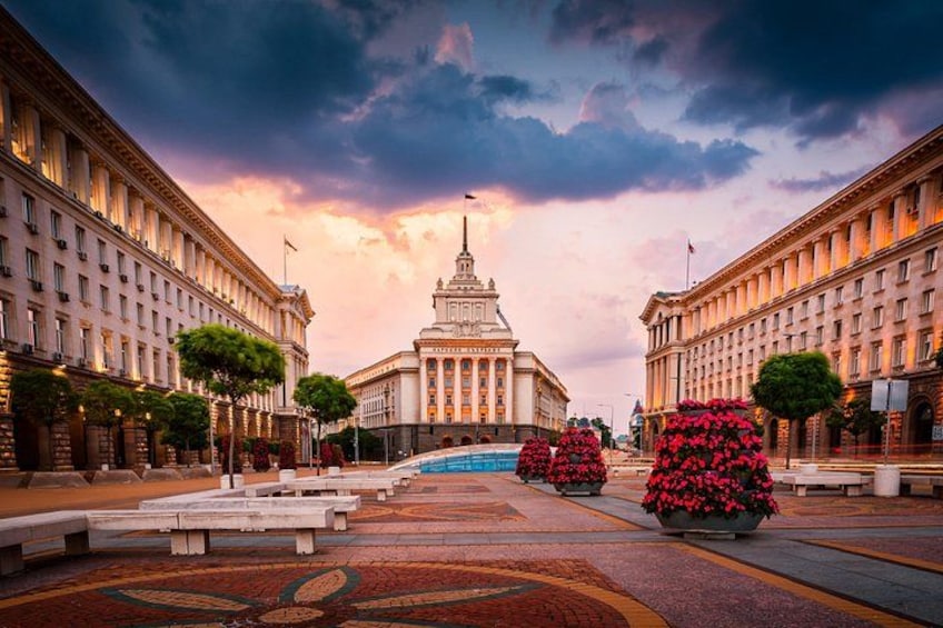 A grand building with a central tower, surrounded by symmetrical architecture and flower arrangements. 2