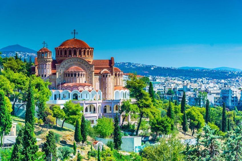 A historic church with a prominent dome and bell towers, surrounded by lush greenery and a cityscape in the background. 1