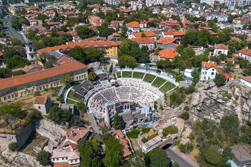 An aerial view of a city with a large circular structure, possibly a stadium, surrounded by residential buildings and greenery. 3