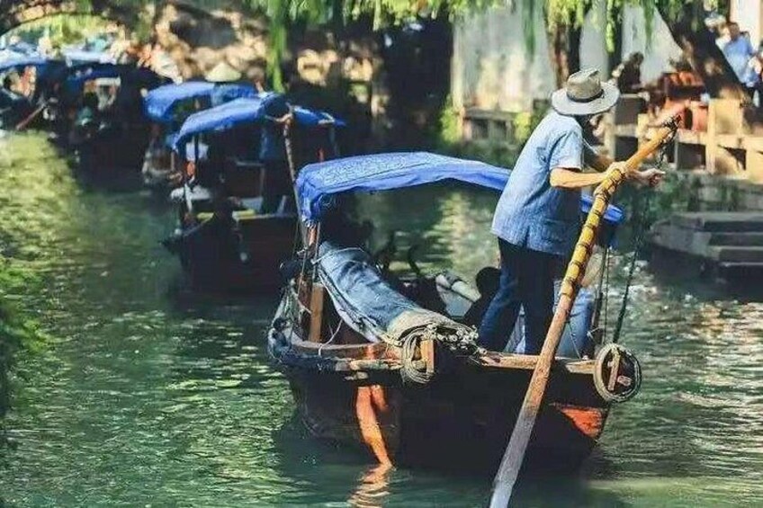A person rowing a traditional boat with a blue tarp on the back, on a calm river. 2