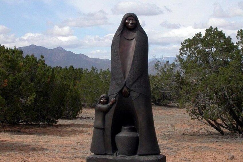Una estatua de una mujer sosteniendo a un niño en un paisaje desértico con montañas al fondo. 5
