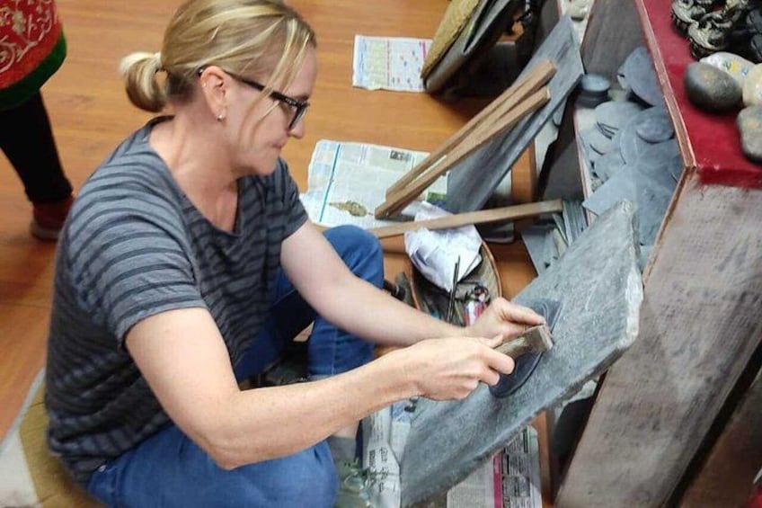 Una persona trabajando con herramientas de piedra, sentada en el suelo, rodeada de diversas rocas y utensilios. 1