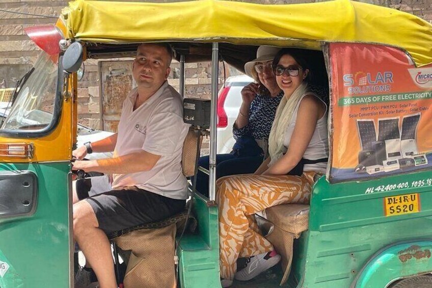 A green auto-rickshaw with a yellow canopy, passengers inside, and a solar panel advertisement on the side. 2
