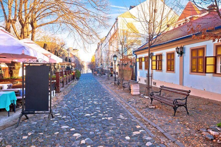 A cobblestone street lined with outdoor cafes and benches. 4