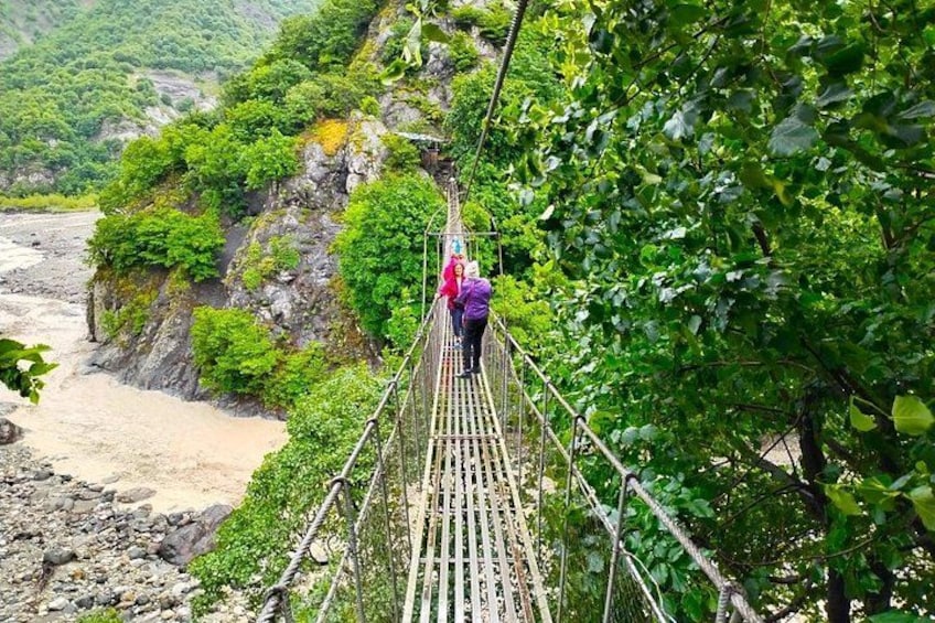 A person walking on a suspension bridge surrounded by lush greenery and a river. 4