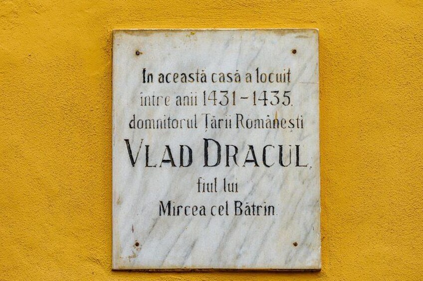 A weathered plaque with text in Romanian, mounted on a yellow wall. 2