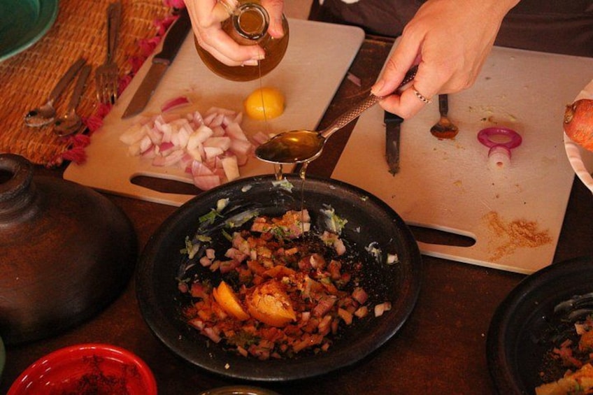 En person hælder væske fra en lille beholder over i en skål med hakkede ingredienser. 2