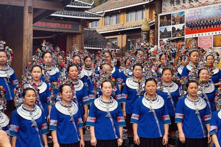 A group of people in traditional attire with elaborate headdresses, standing in front of a building with traditional architecture. 5