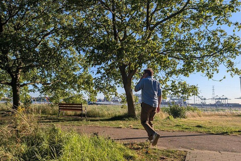A person jogging on a path, a bench, and trees in a park with a view of a distant industrial area. 2