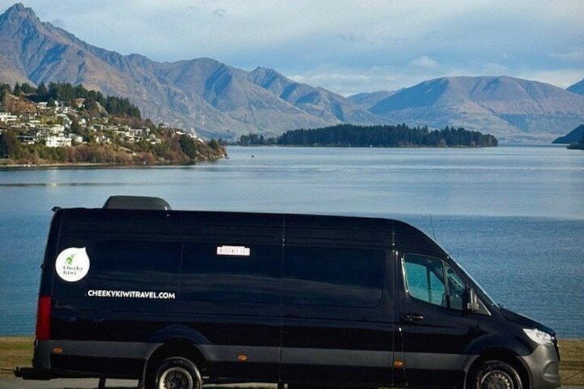 A black van parked by a lake with mountains in the background. 2