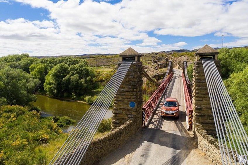 A stone bridge with metal railings, a car on the bridge, and a river below. 4
