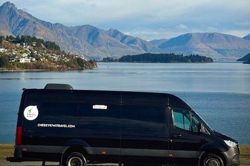 A black van parked by a lake with mountains in the background. 2