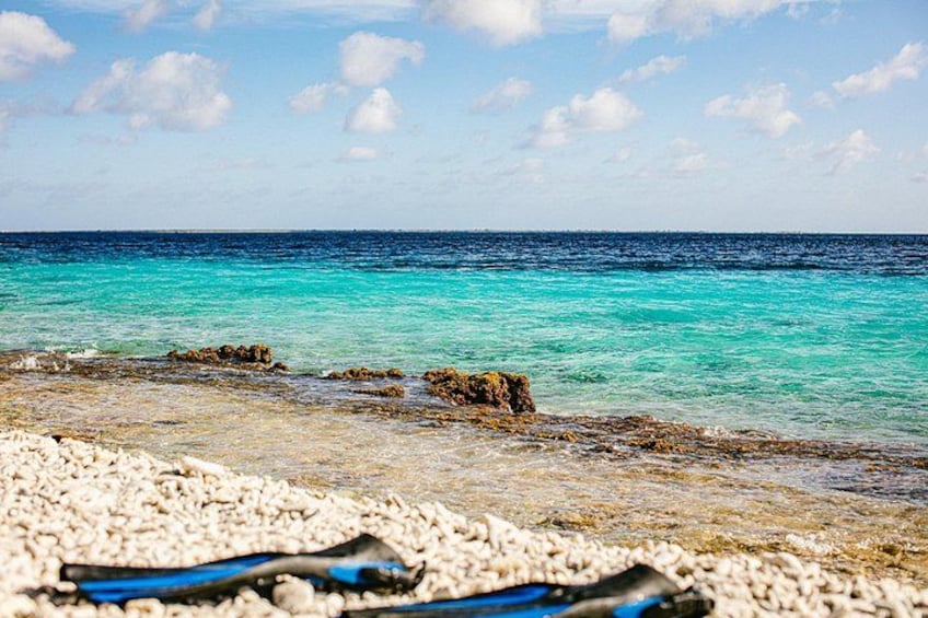 A beach with clear turquoise water, pebbles, and rocks. 3