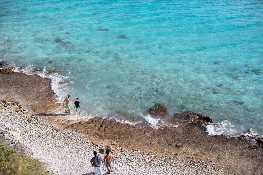 A rocky beach with clear turquoise water, people standing on the shore, and a rocky shoreline. 4
