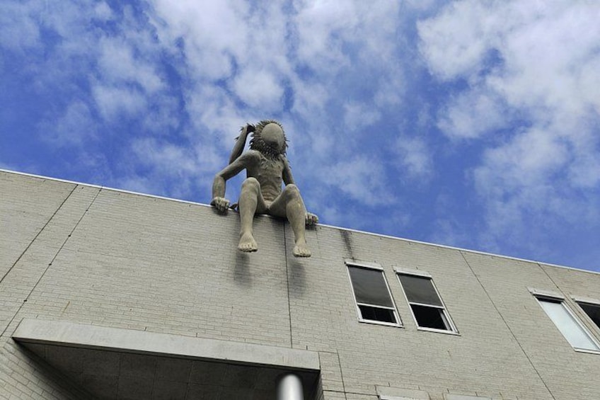 A statue of a person sitting on a building's ledge with a blue sky in the background. 2