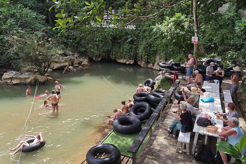 A riverside scene with people floating on tubes, a dock with tables, and a natural, wooded backdrop. 3