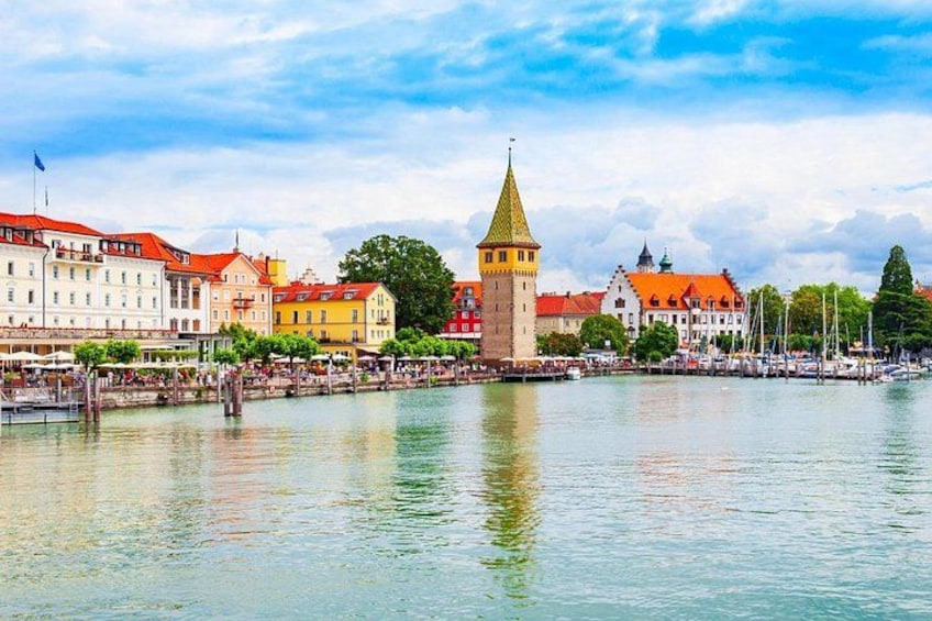 En by ved floden med historiske bygninger, et markant tårn og et roligt vandareal, der spejler arkitekturen. 3
