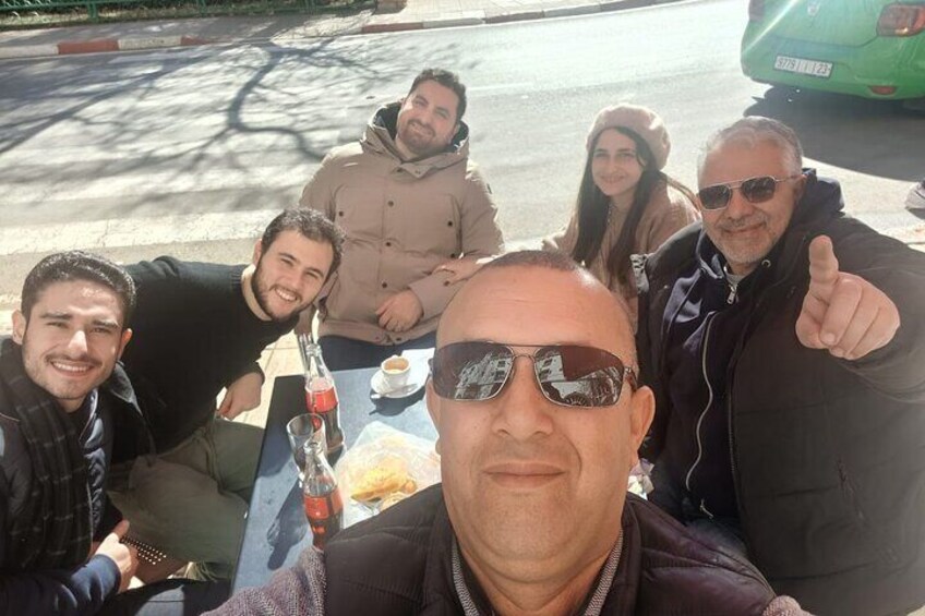 A group of people sitting at a table outdoors with a bottle and a plate of food. 4