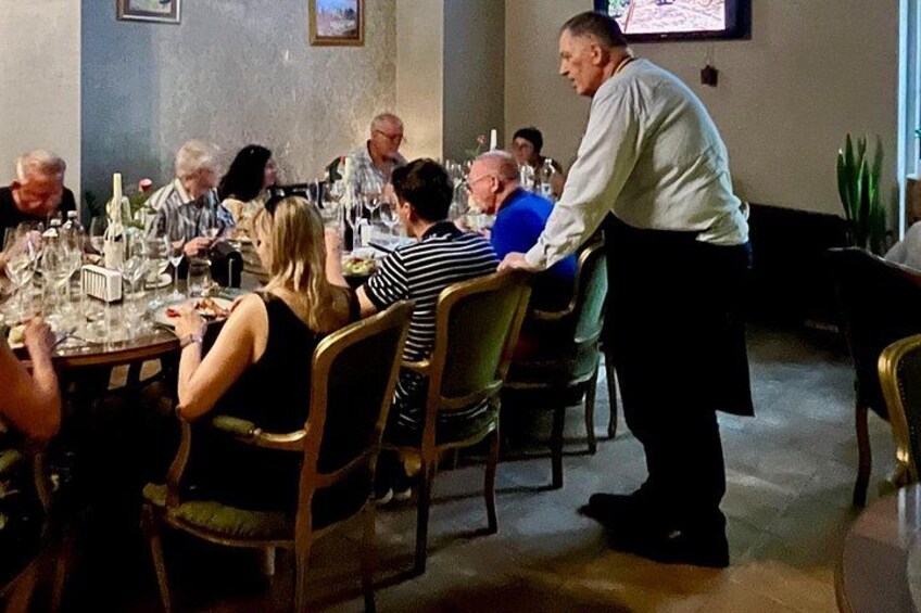 Ein Restaurant mit Gästen an Tischen, einem Kellner, der die Gäste bedient, und einem an der Wand befestigten Fernseher. 5