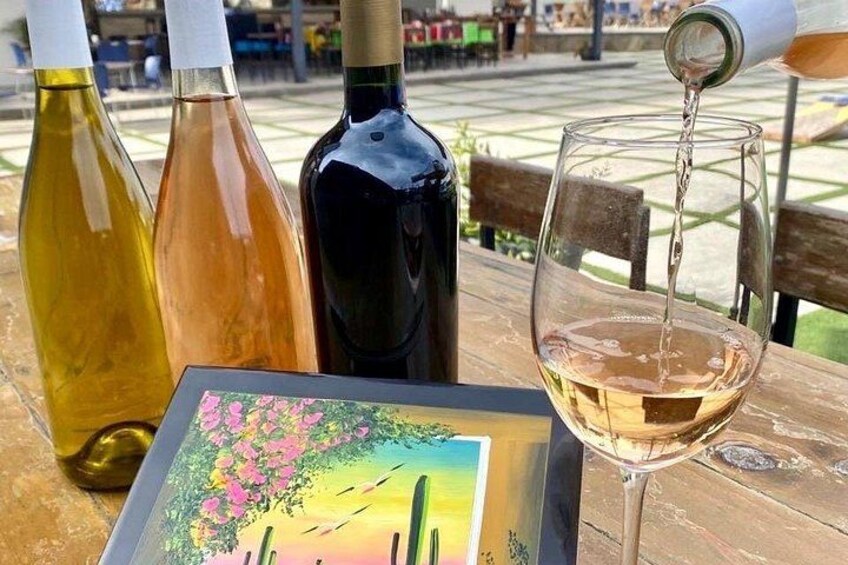 Three wine bottles and a glass on a table with a colorful painting. 2