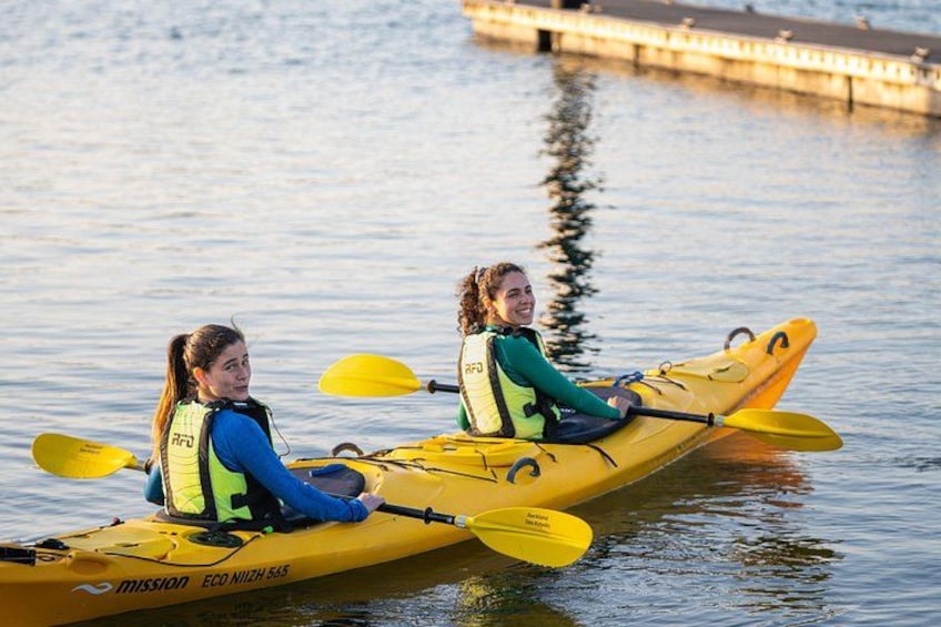 Two people kayaking on a calm body of water with a dock in the background. 2