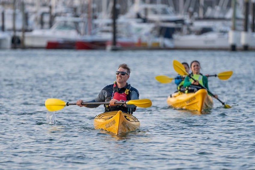 Two kayakers in yellow kayaks on a calm body of water with a marina in the background. 4