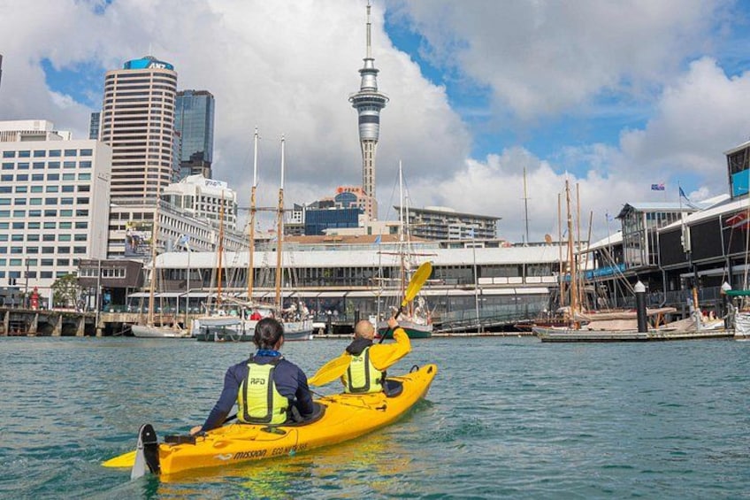 Two people kayaking on a body of water with a city skyline in the background. 3