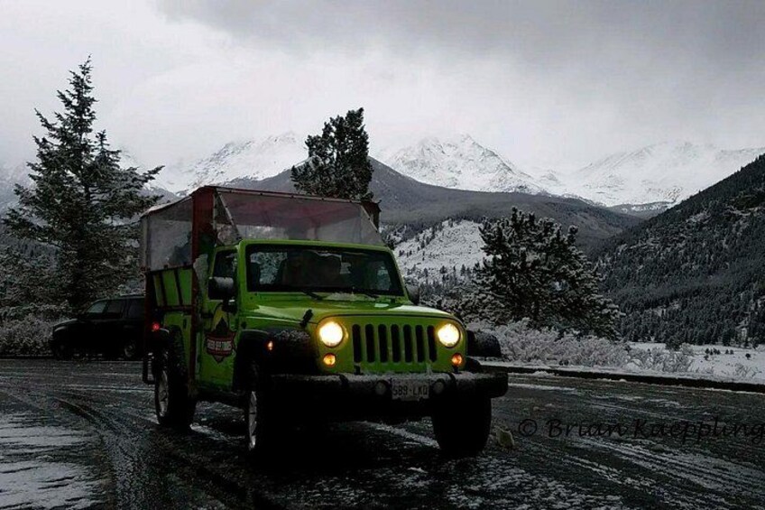 Un véhicule tout-terrain vert est garé sur une route mouillée, avec des montagnes enneigées en arrière-plan. 3