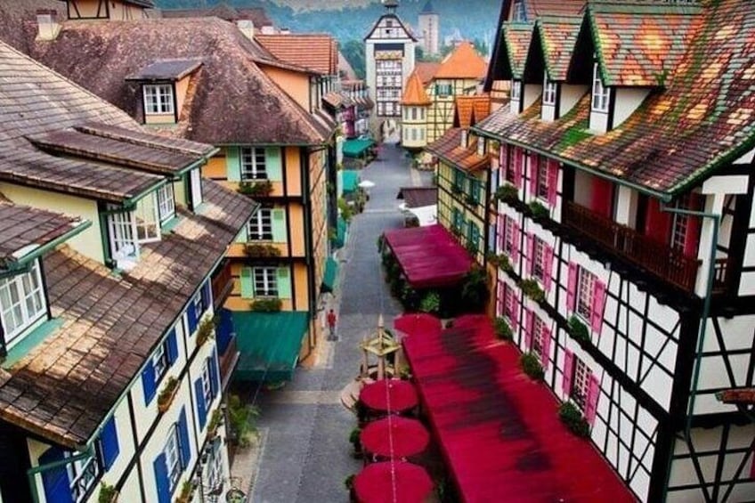 Een smalle straat met kleurrijke vakwerkhuizen, een rood luifje en een kerk in de verte. 2
