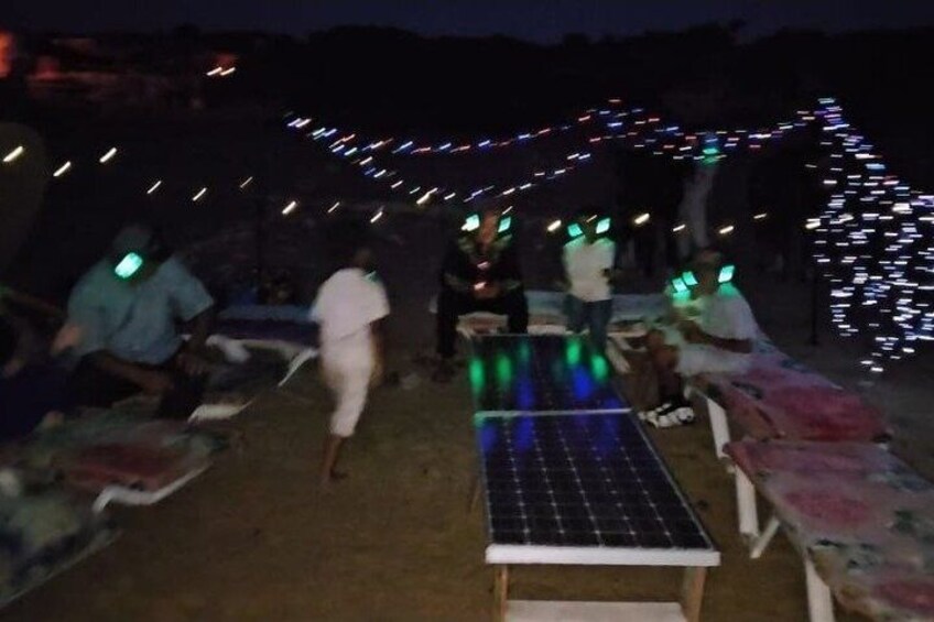 People sitting on benches under string lights at night. 4