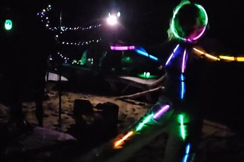 A person illuminated with colorful lights, a sandy area, and a vehicle in the background. 3